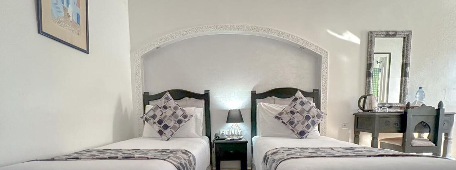 Una cama doble con cabecera arqueada, dos mesitas de noche con lámparas, un espejo y un tocador con espejo.