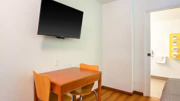 A room with a wooden table and chairs, a flat-screen TV mounted on the wall, and a door leading to a bathroom with a towel rack.