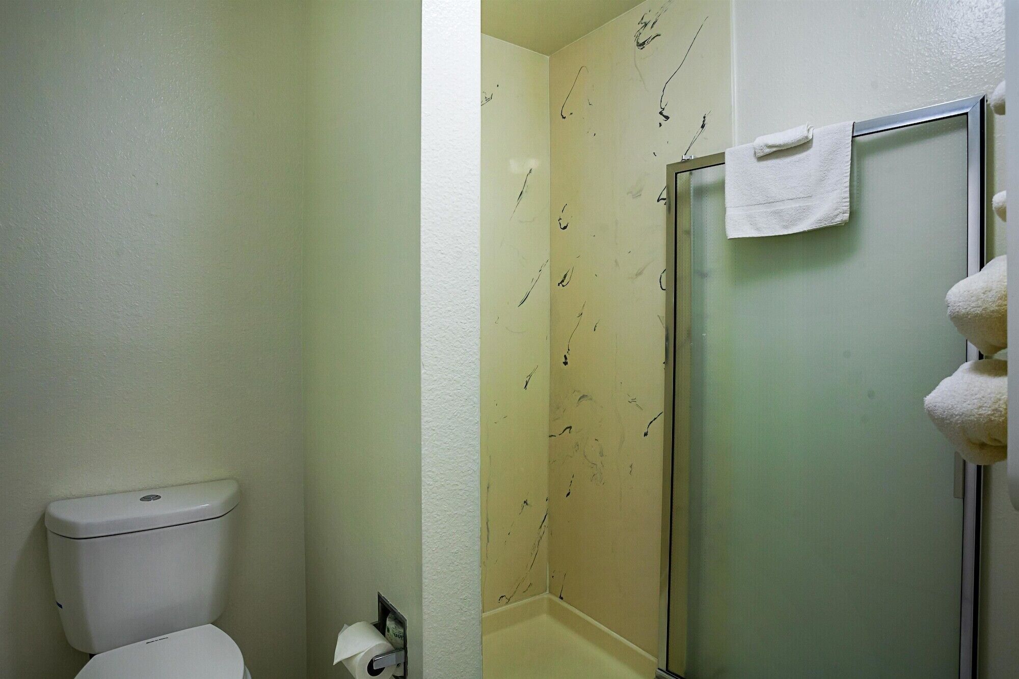 Une salle de bain équipée de toilettes, d’une douche à parois de verre et d’un porte-serviettes.