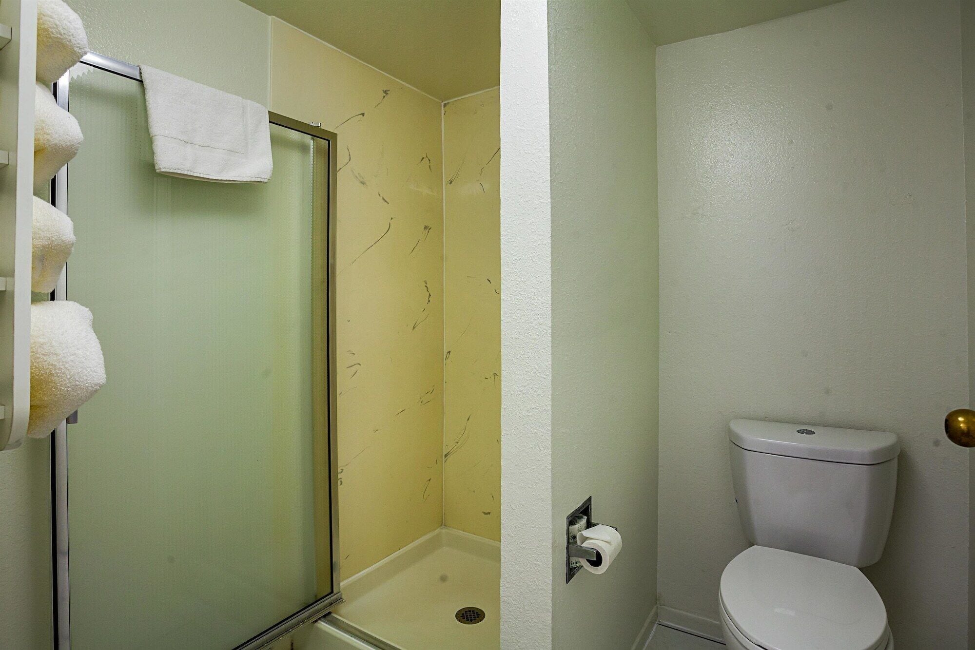 Een badkamer met een glazen douchedeur, een toilet en een handdoekrek met meerdere handdoeken.
