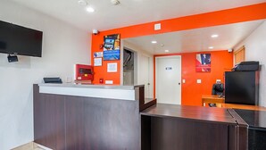 Un espace d’accueil comprenant un comptoir de réception en bois, un téléviseur à écran plat fixé au mur et un kiosque numérique.