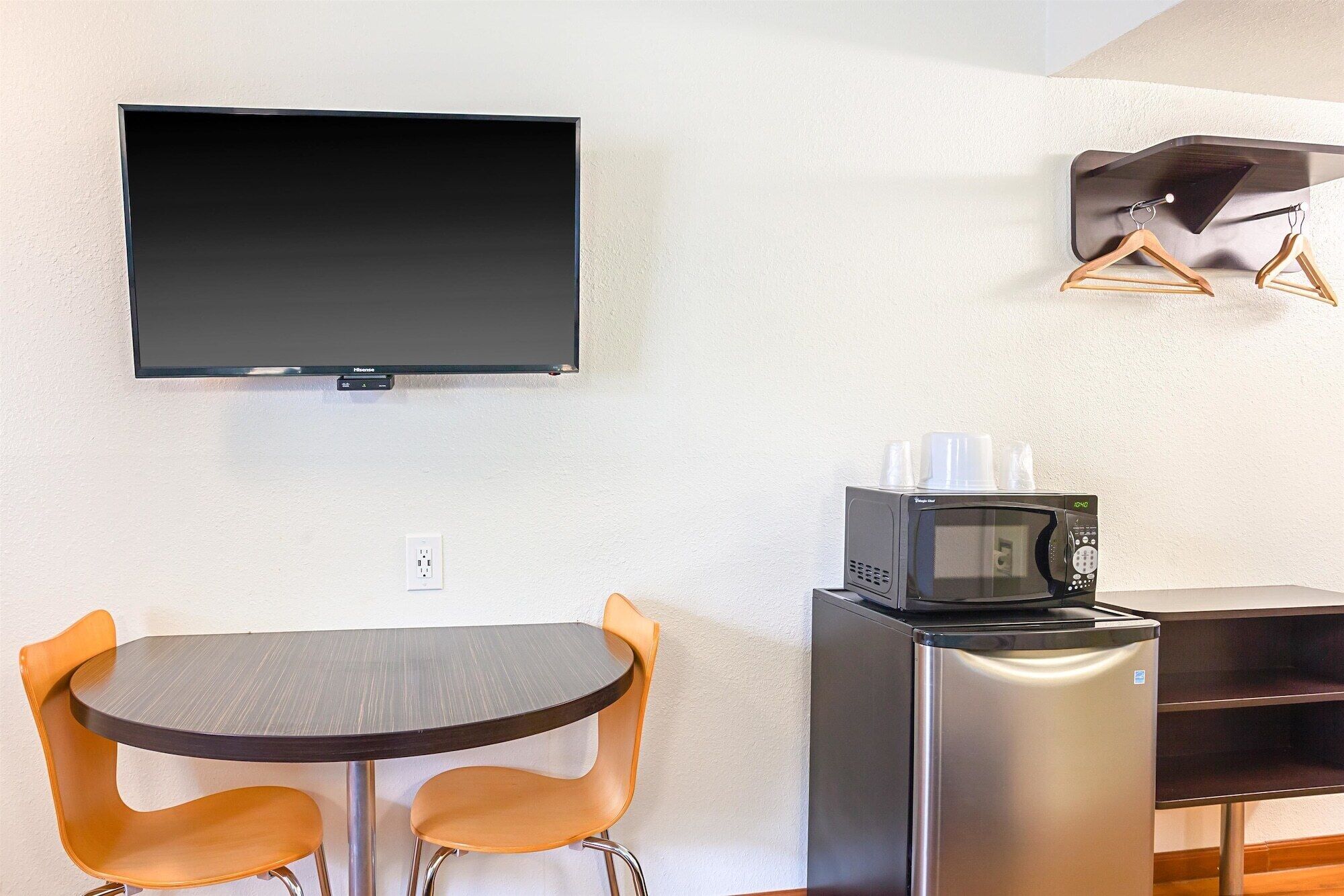 A compact kitchenette with a flat-screen TV, a microwave, and a refrigerator. There is a small round table with two chairs.