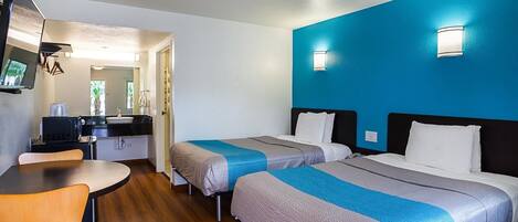 Habitación de hotel con dos camas, un escritorio, una silla, un televisor y un baño visible a través de una puerta abierta.