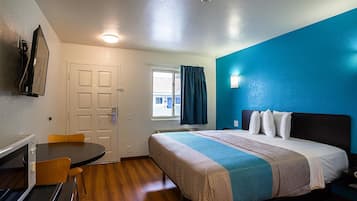 A hotel room with a bed, a desk, a chair, and a window with curtains.