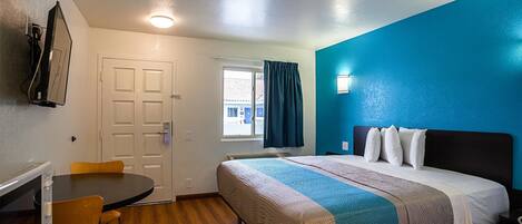 A hotel room with a bed, a desk, a chair, and a window with curtains.