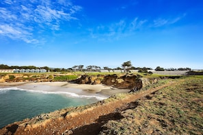 A coastal landscape with a beach, cliffs, and a row of buildings in the background.