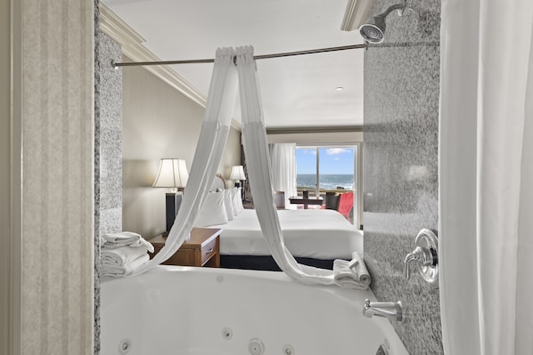 A modern hotel room with a large bathtub, two beds, a view of the sea, and a balcony.