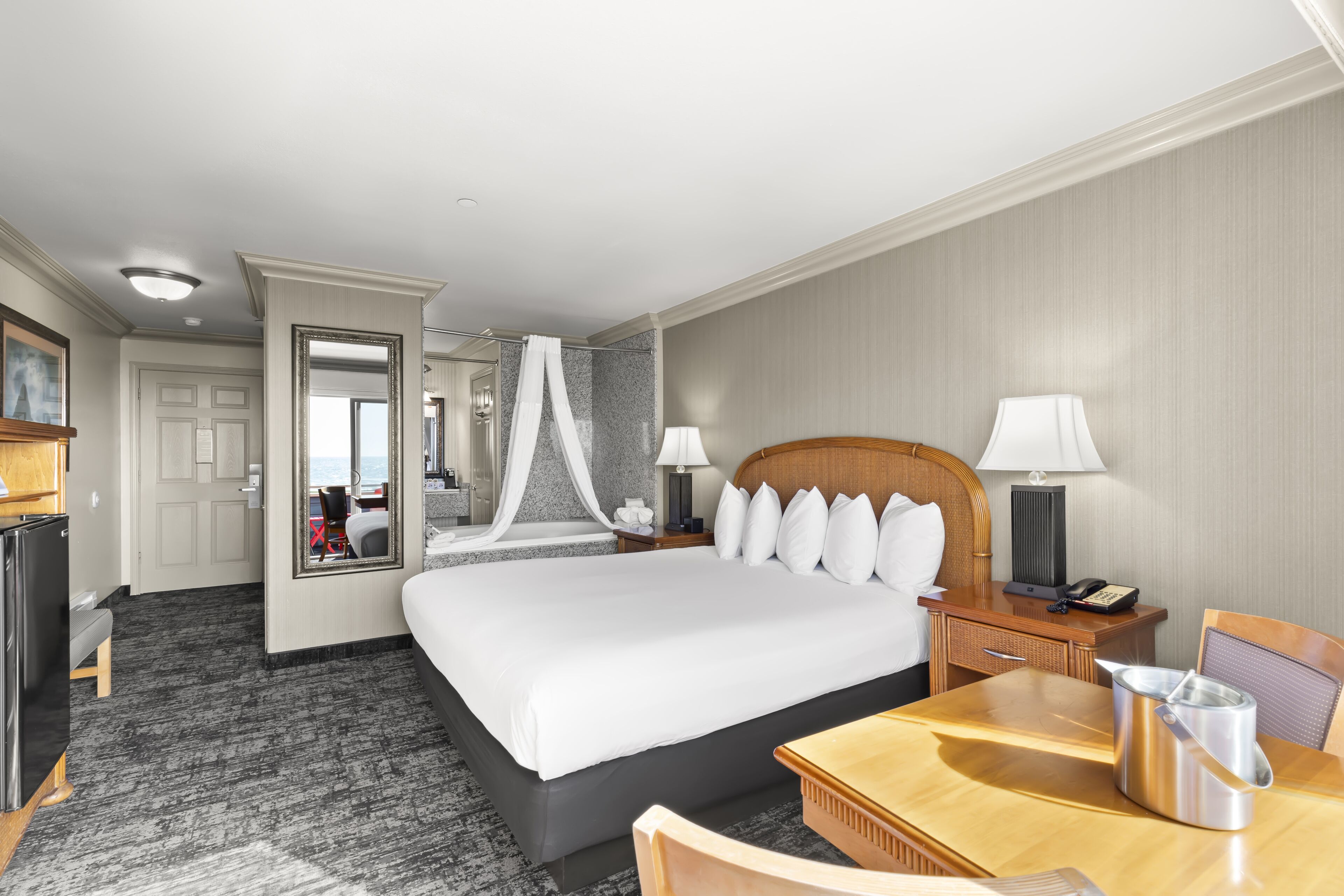 Habitación de hotel con una cama grande, lámparas de noche, una mesita de noche de madera, un escritorio con una silla y un minibar.