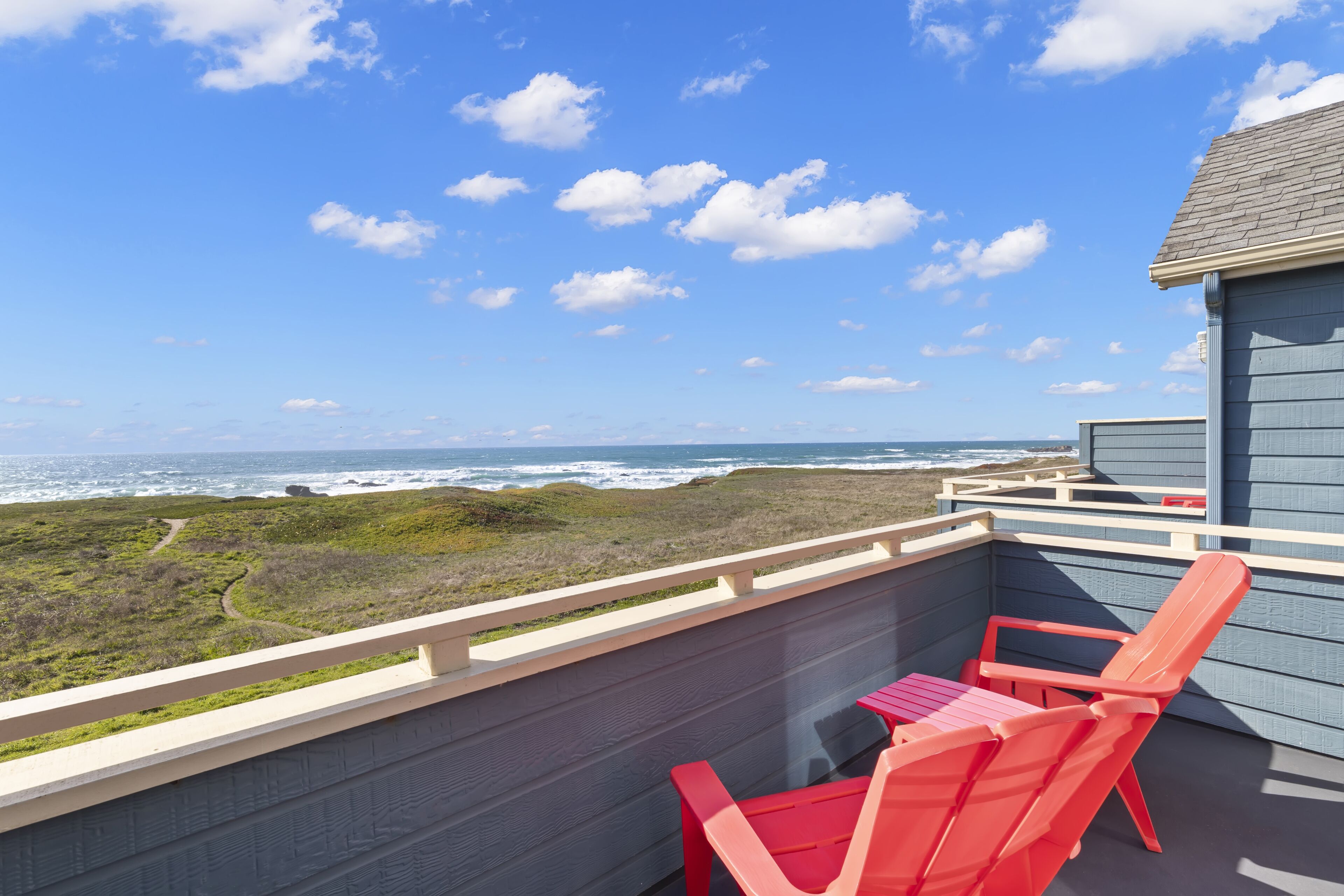 A balcony with red chairs and a table overlooking a coastal landscape.