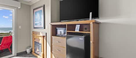 Habitación con televisor de pantalla plana grande, microondas integrado, refrigerador, chimenea y vista al océano a través de una puerta corrediza de vidrio.
