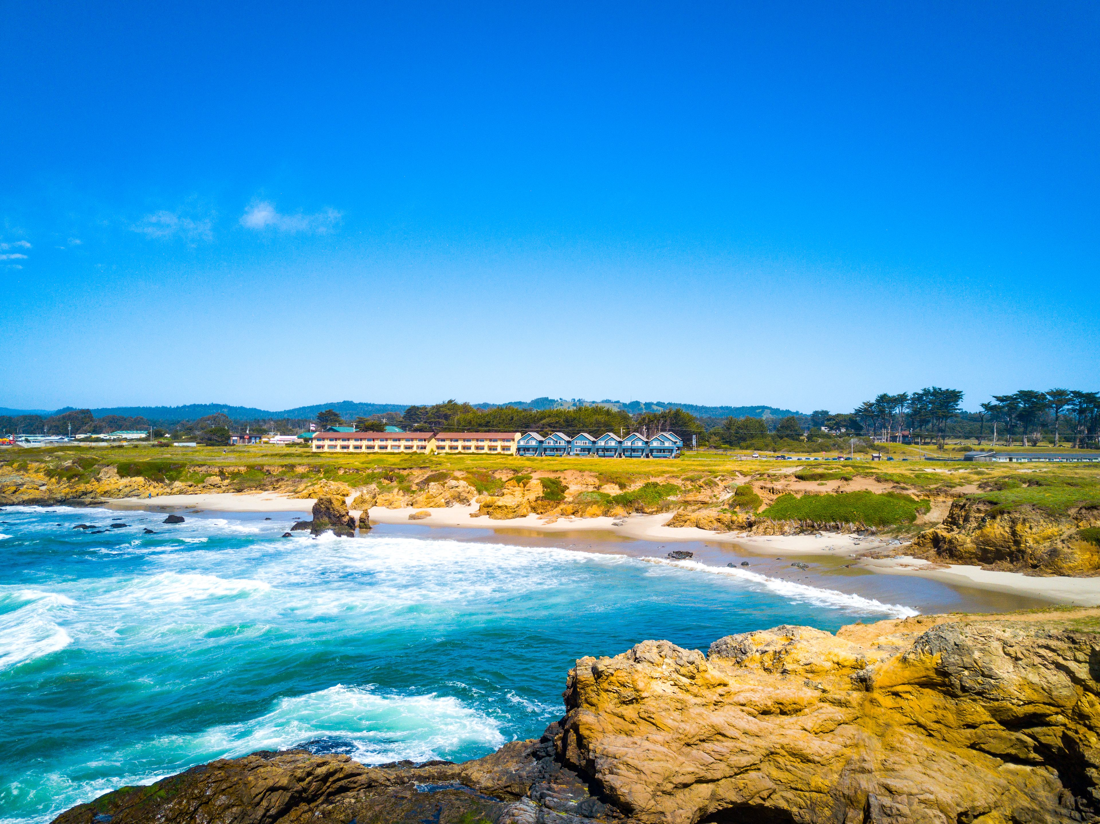 A coastal hotel with multiple blue buildings, a rocky shoreline, and a view of the ocean.