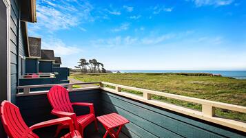 A balcony with red chairs and a small table, overlooking a grassy area and the ocean.