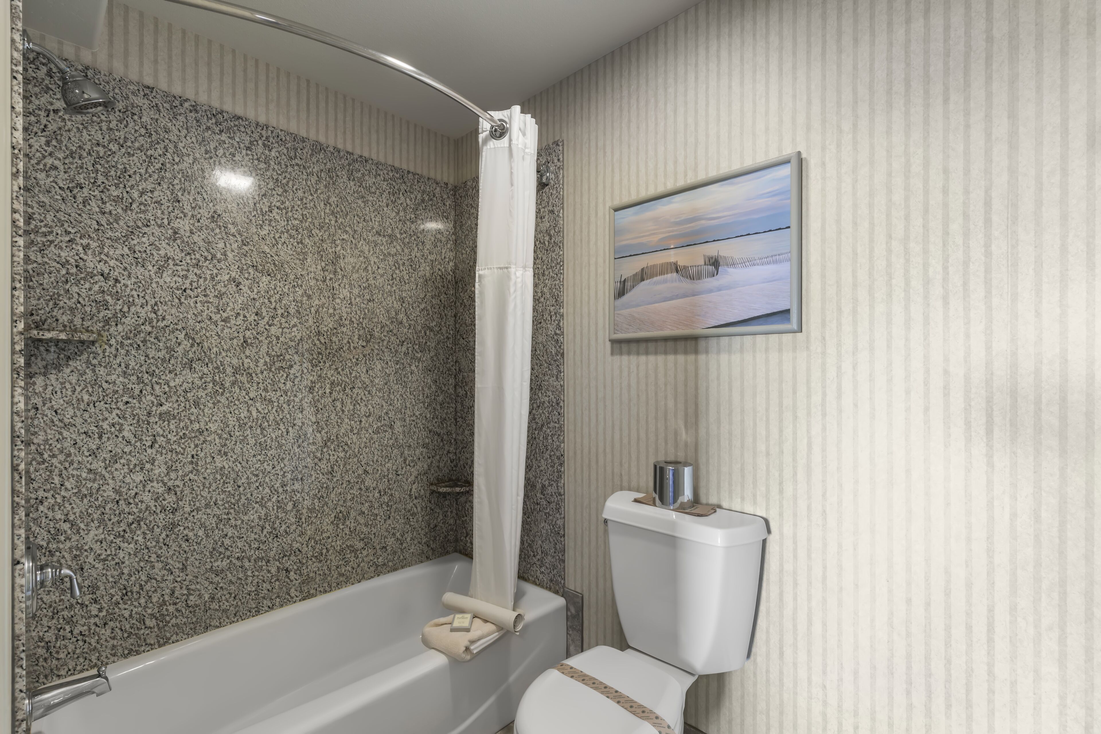 A bathroom with a granite shower wall, a bathtub, and a toilet.