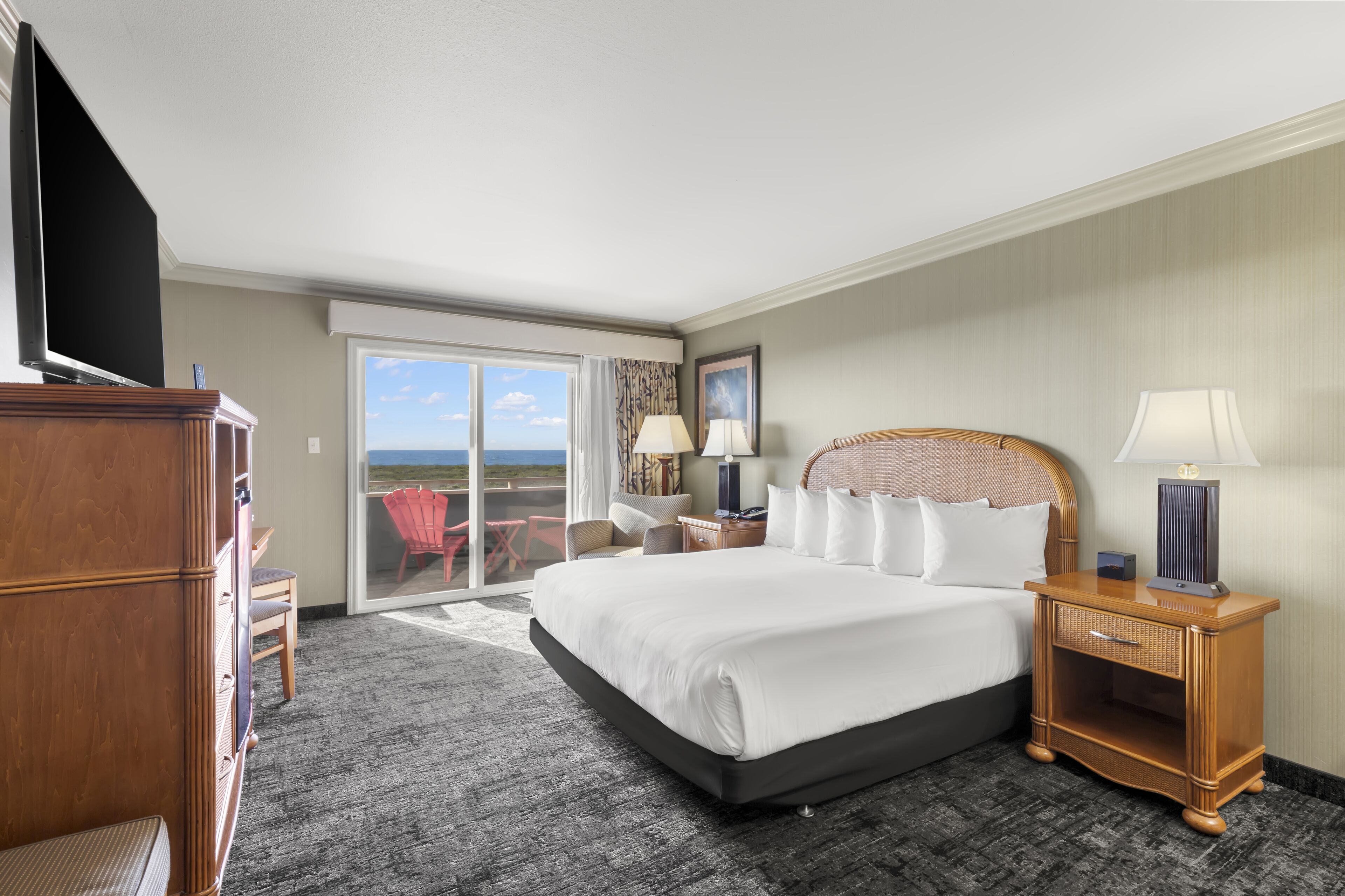 A hotel room with a large bed, a flat-screen TV, a wooden nightstand, a chair, and a view of the outdoors.