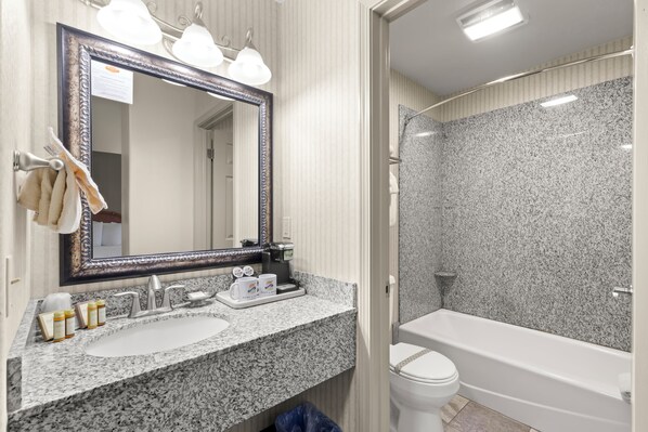 Un baño con encimera de granito, un espejo grande, un lavamanos blanco, un inodoro y una bañera.