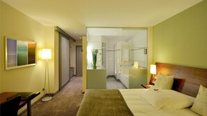 Een hotelkamer met een bed, nachtlampjes, een bureau, een stoel, een spiegel en uitzicht op de badkamer.