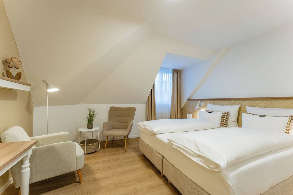 A hotel room with a bed, a chair, a small table, and a potted plant.