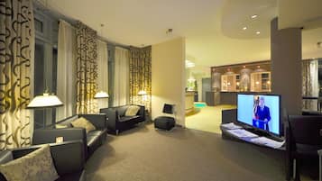 Un moderno vestíbulo de hotel con zona de estar, mostrador de recepción y un televisor que muestra un noticiero.