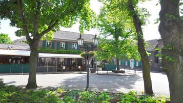 Une rue bordée d’un bâtiment doté d’une grande fenêtre et d’une porte, entouré d’arbres et agrémenté d’un jardinier avec des fleurs.