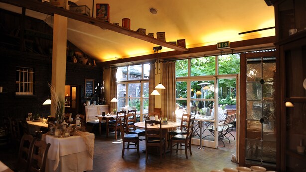 Een gezellig restaurant met houten tafels en stoelen, grote ramen en een warme inrichting.