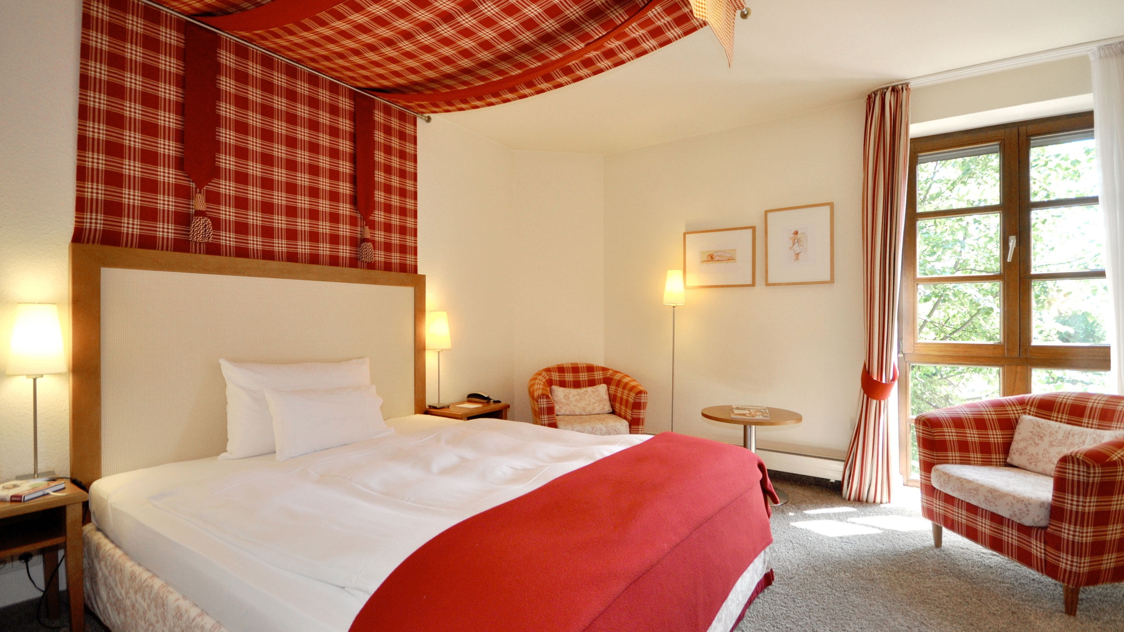 A hotel room with a large bed, a chair, a small table, and a window with curtains.