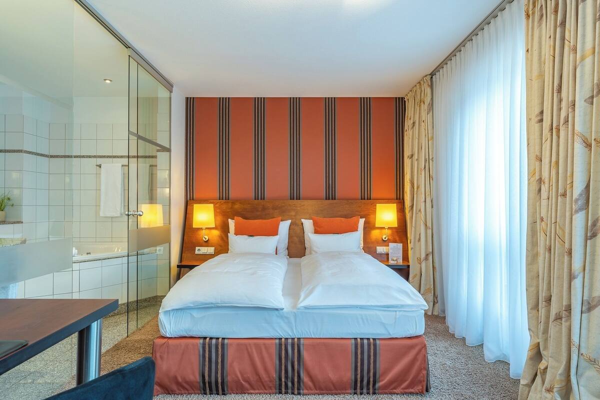 A hotel room with a large bed, a glass shower enclosure, and a wooden headboard.