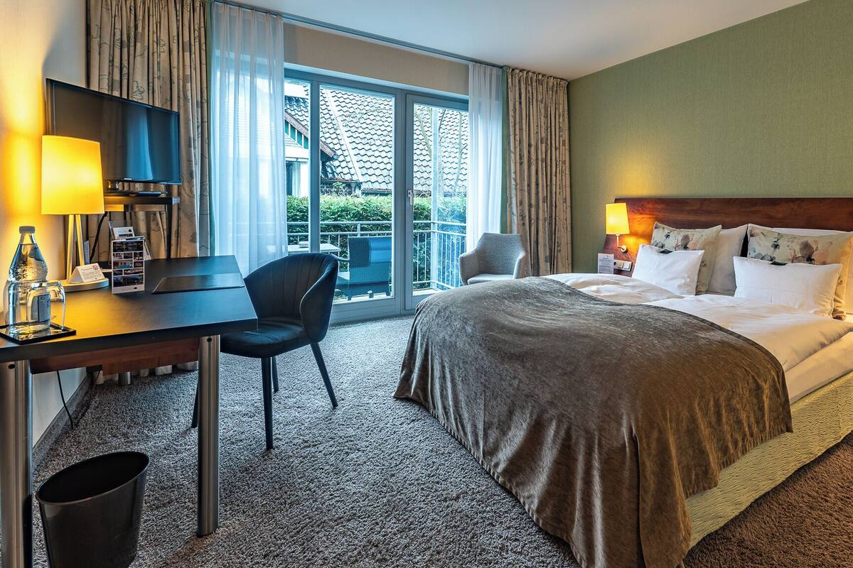 A hotel room with a bed, desk, chair, and a view of the outside.