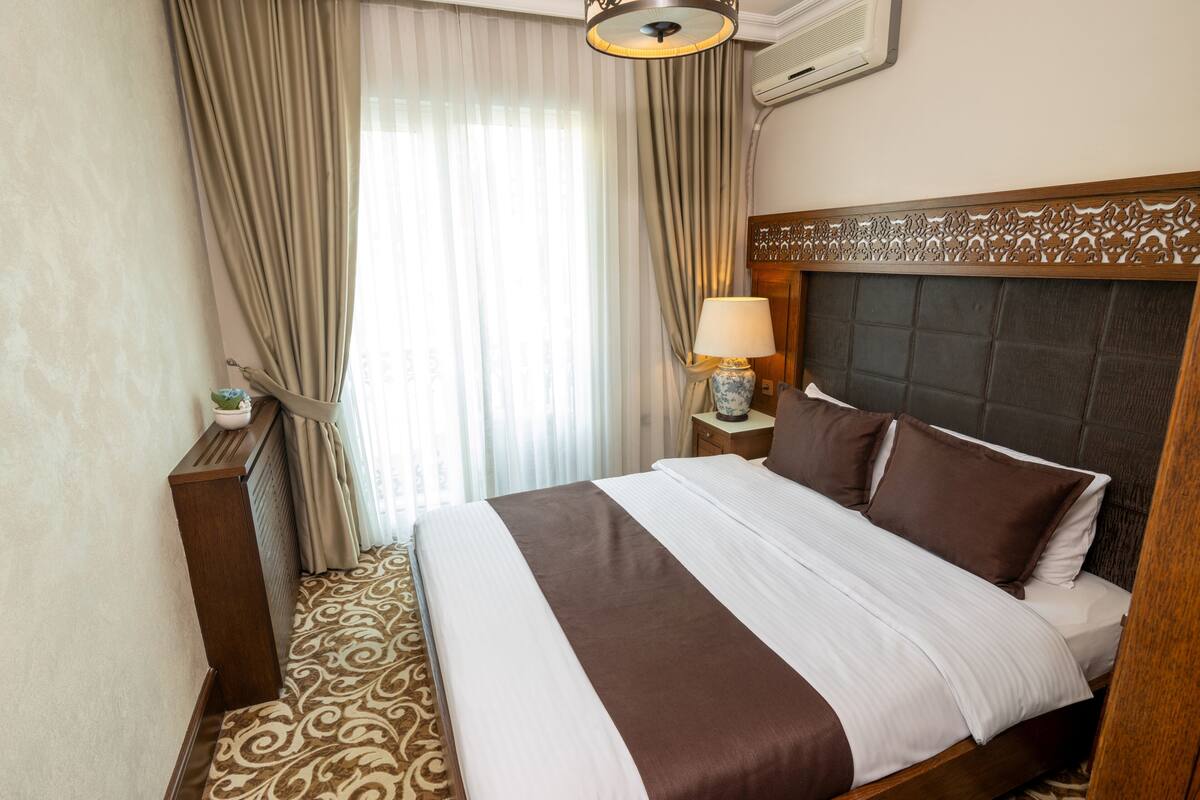 A hotel room with a large bed, a nightstand, a lamp, and a window with curtains.