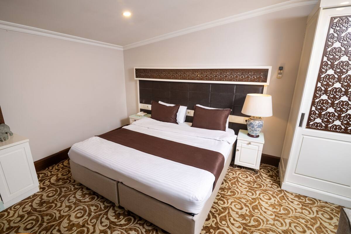 A hotel room with a large bed, a nightstand with a lamp, and a decorative headboard.