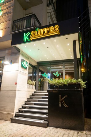 Entrada de un hotel con un letrero de neón que dice "K SUITES" y una gran "K" en los escalones.