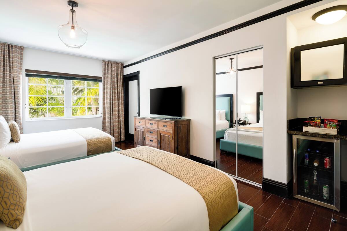 Ein Hotelzimmer mit zwei Betten, einem Fernseher, einer Minibar und einer Schiebetür zu einem Badezimmer.