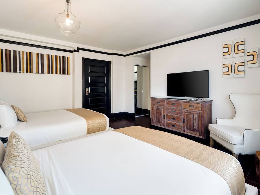 Habitación de hotel con dos camas, un televisor, un armario de madera y una silla.