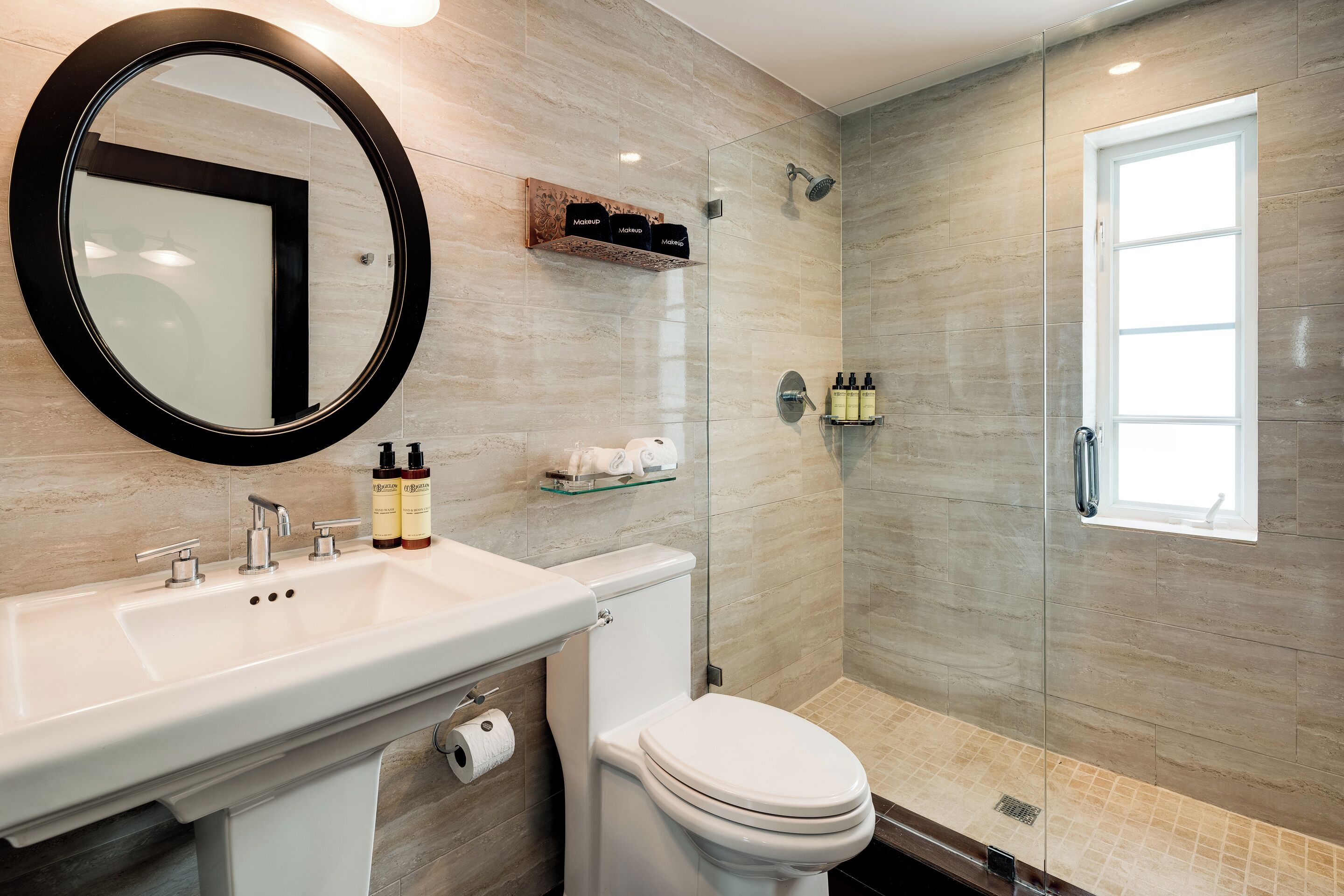 A modern bathroom with a round mirror, a white sink, a toilet, and a glass-enclosed shower area.
