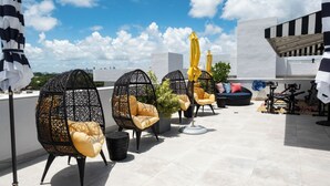A rooftop terrace with black wicker chairs, yellow cushions, and a potted plant. - Hotel Croydon (Miami Beach)