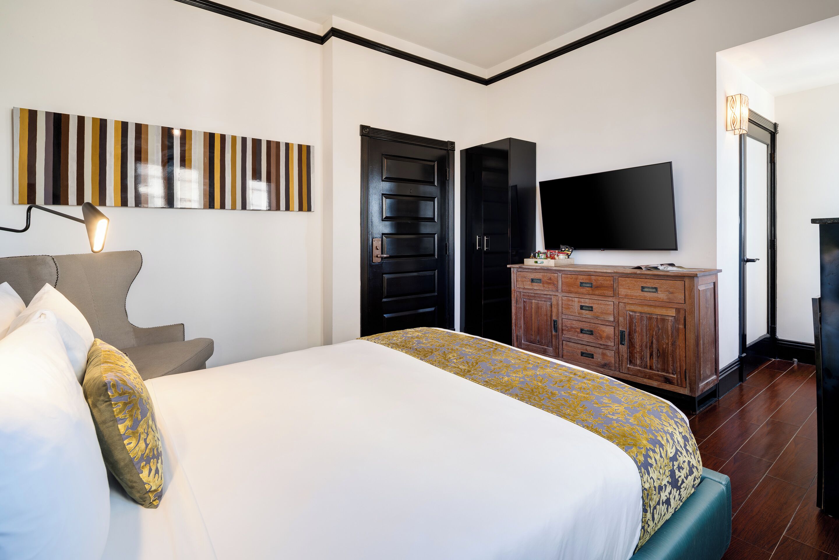 Una habitación de hotel con cama, televisión, armario y un cuadro en la pared.