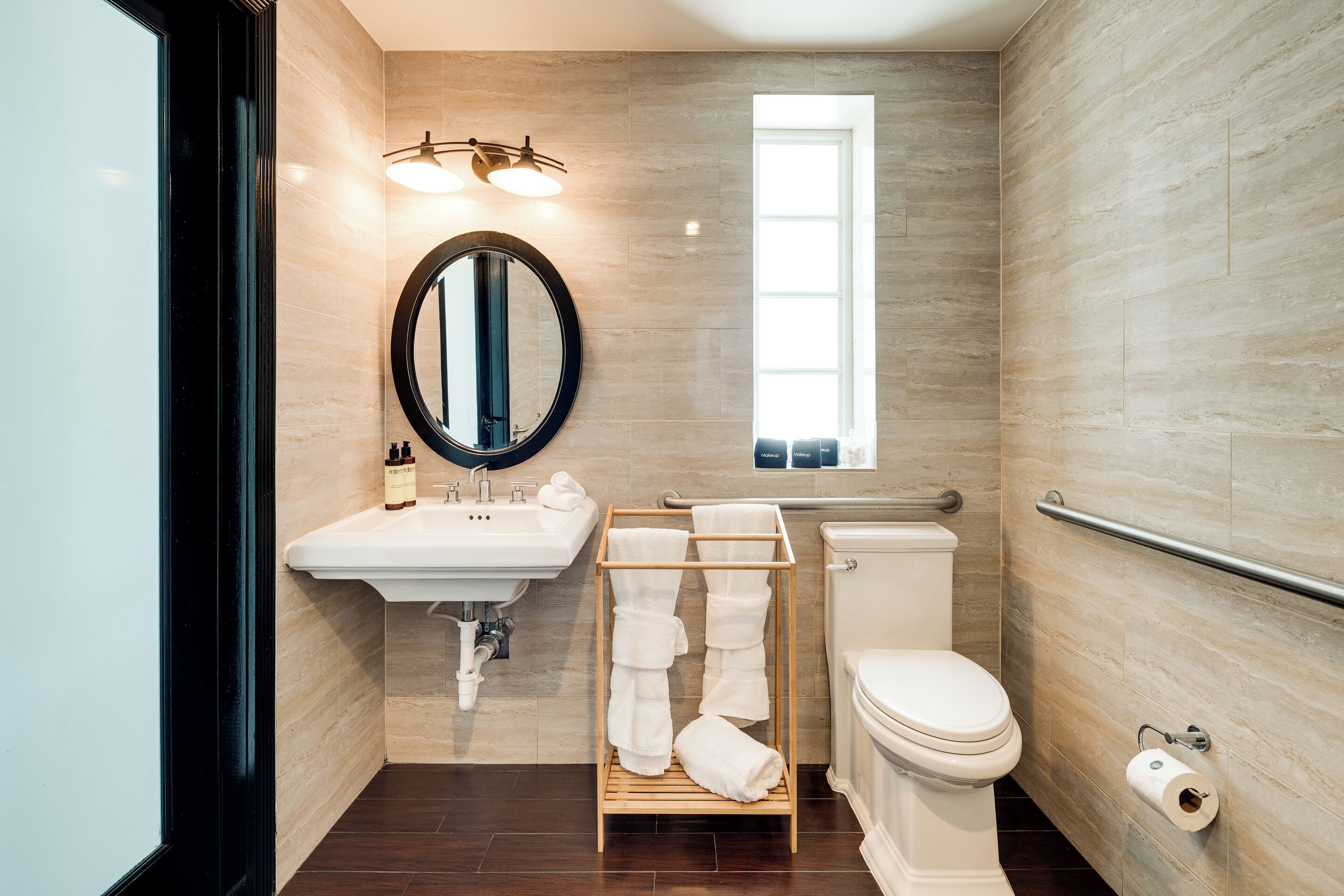 Een moderne badkamer met een wastafel, spiegel, handdoekrek, toilet en een raam.