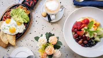 Un desayuno con un plato de huevos, aguacate y tostadas, una taza de café y un tazón de ensalada de frutas.