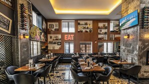 A restaurant with a central 'EAT' sign, black leather seating, patterned floor tiles, and various wall decorations including framed pictures and a TV screen. - Hotel Croydon (Miami Beach)
