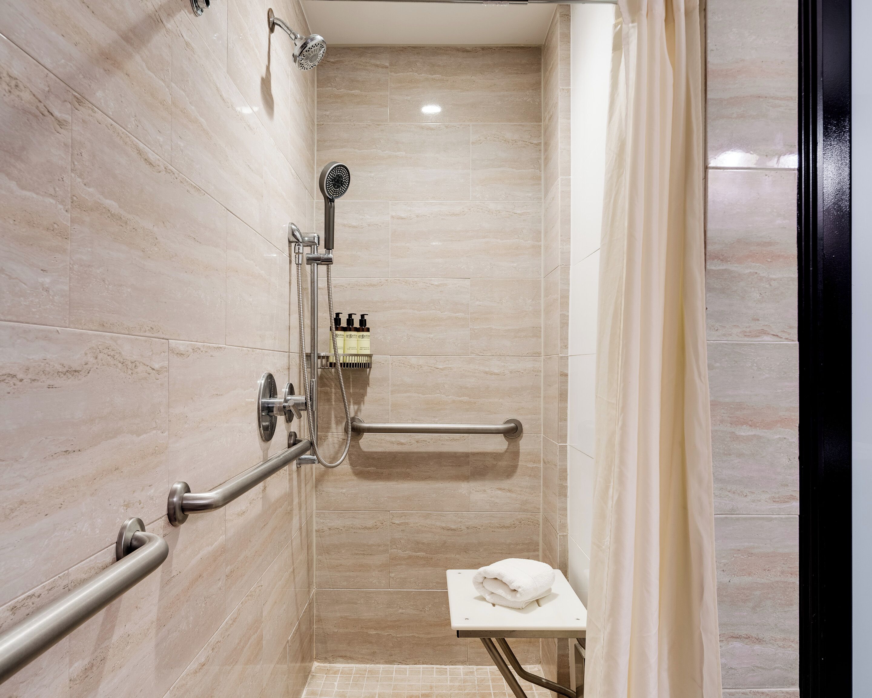 A modern shower with a handheld showerhead, a built-in seat, and a towel rack.