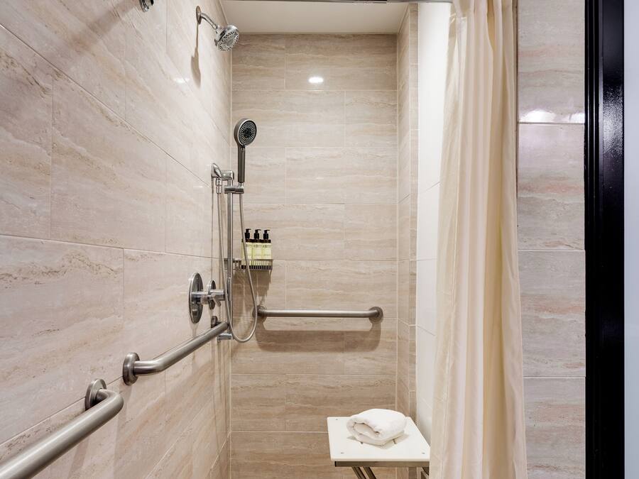 A modern shower with a handheld showerhead, a built-in seat, and a towel rack.