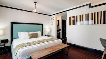 A modern hotel room with a large bed, a wooden bench, a desk, and a wall-mounted artwork.
