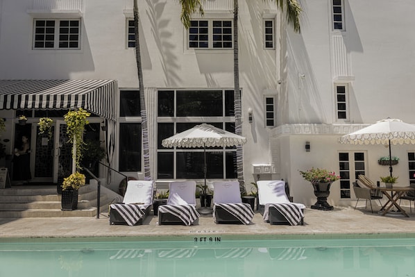 Una piscina al aire libre, sombrillas, sillones reclinables de piscina