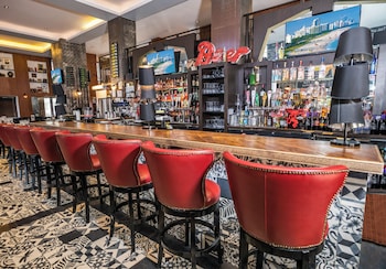 A lobby with a patterned carpet, white leather chairs, a reception desk, and a television screen. at Hotel Croydon