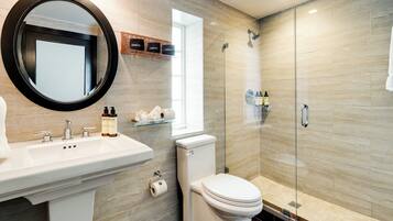A modern bathroom with a round mirror, a sink with two faucets, a toilet, and a glass-enclosed shower area.