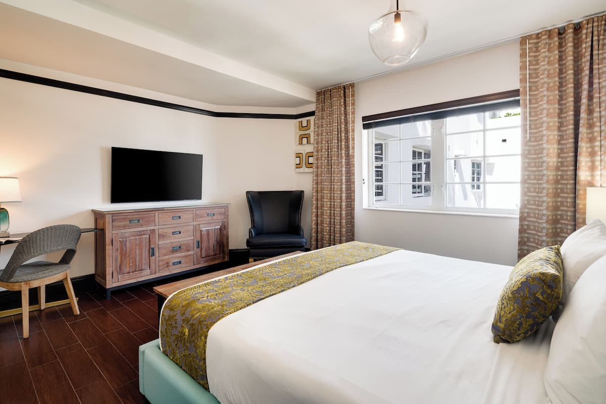 Ein Hotelzimmer mit Bett, Fernseher, Schreibtisch mit Stuhl und Fenster mit Vorhängen.