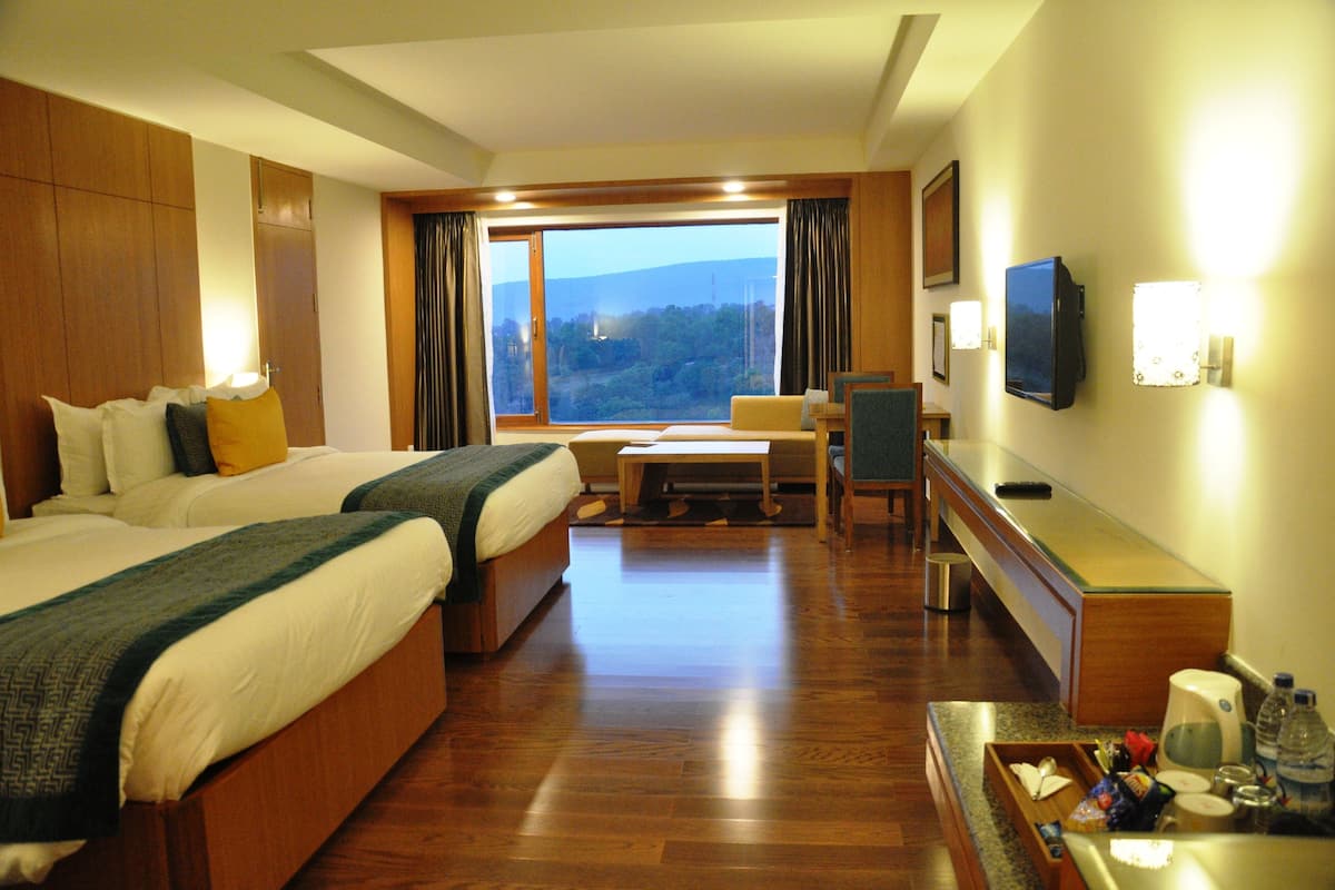 A hotel room with two beds, a desk, a television, and a view of the outdoors.