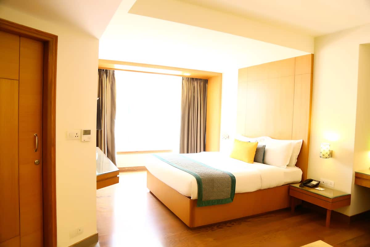 A hotel room with a large bed, bedside tables, a nightstand, and a window with curtains.