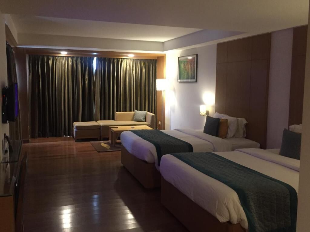 A hotel room with two beds, a sofa, a flat-screen TV, and a large window with curtains.