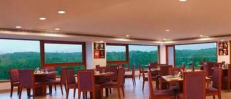 A spacious dining area with wooden tables and chairs, large windows offering a view of the outdoors.
