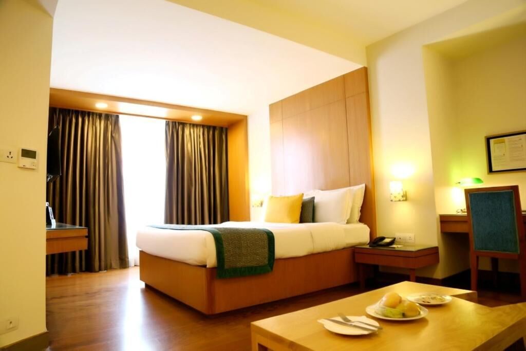 A hotel room with a bed, bedside table, chair, and a small dining table with plates.